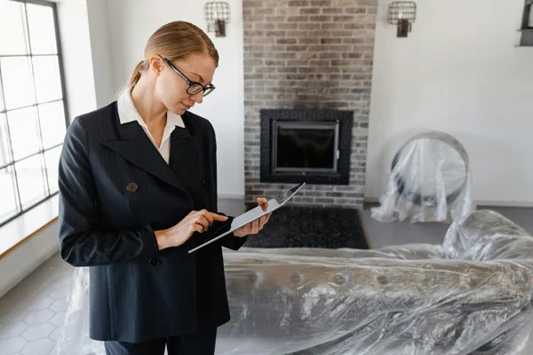 Woman in a suit standing in a home with a fireplace looking a clipboard with frequently asked questions about real estate appraisals