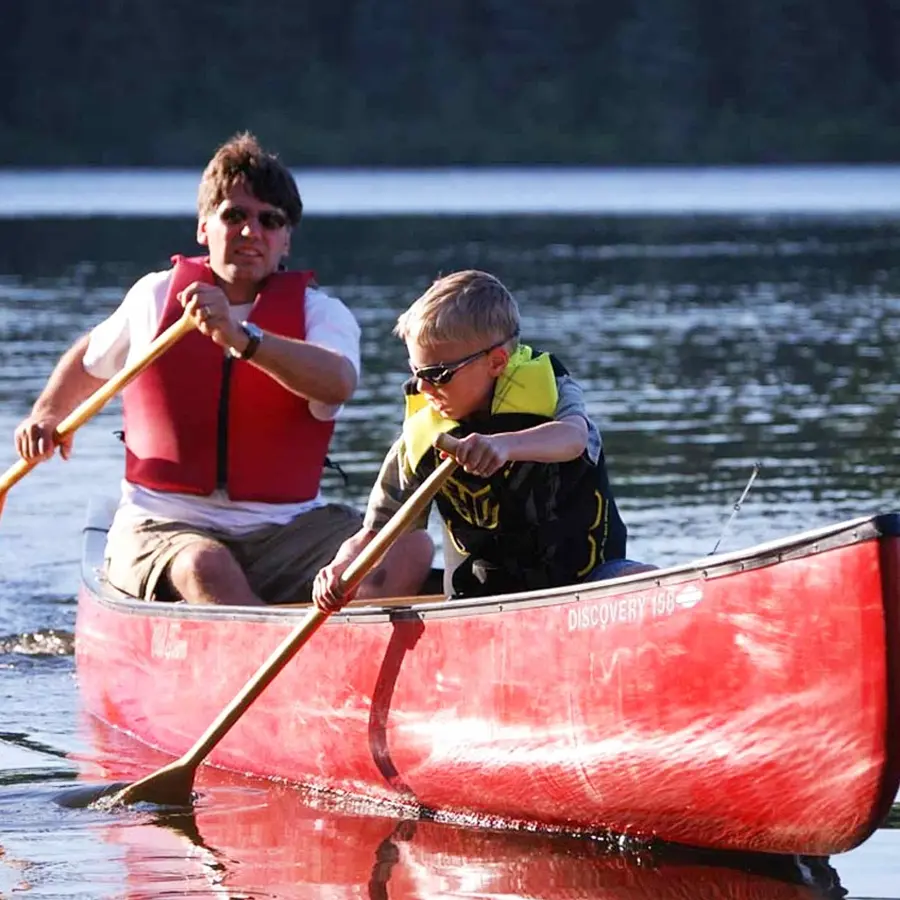 A man and young boy wearing life preservers and sunglasses while paddling a red canoe